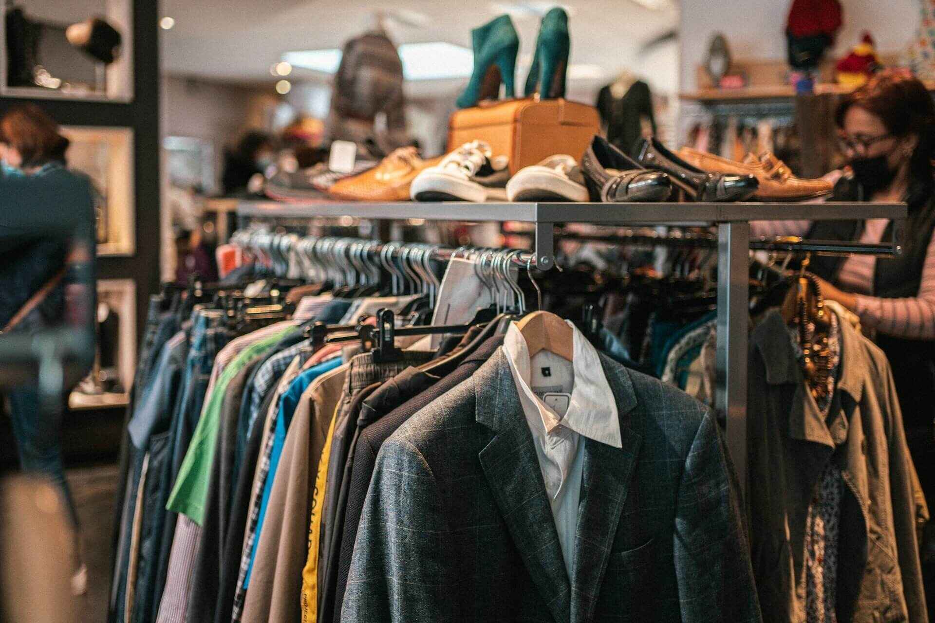 Clothes hanging on a rack with shoes displayed on top in a store.